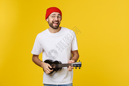 在黄金背景上被孤立的 有趣的年轻人玩吉他的特快节目歌曲男性吉他手艺术家乐趣微笑黑色青年音乐家岩石图片