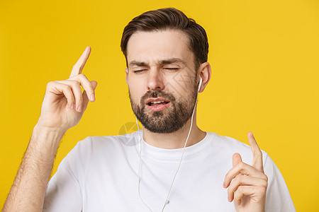 一个年轻男人的帅气 享受着黄色背景的音乐技术成人男生白色微笑耳机幸福男性闲暇衬衫图片