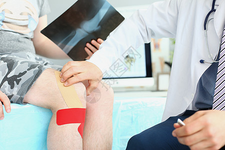 医生穿制服和听诊器 仔细检查病人的腿部录音男人愈合保健磁带诊所胶合膝盖身体客户图片
