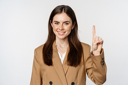 公司女性的肖像 女售货员展示一号手指和微笑 站在白色背景的西装上图片