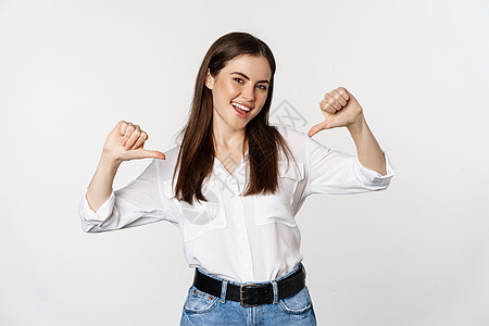 年轻女性的肖像指着自己 自我促进 站在白背景上站立顾问商务快乐人士企业家管理人员女孩商业成人微笑图片