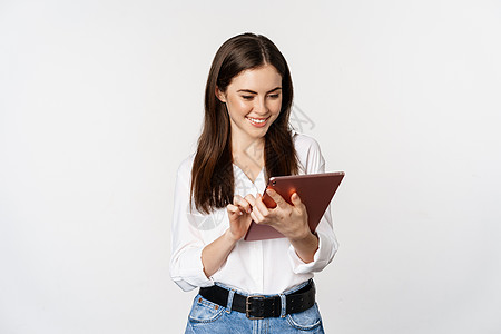 看着数字平板电脑 工作 站立在白色背景之上的 微笑着的女性公司的肖像商业售货员成人职业工作室广告顾问促销女孩办公室图片
