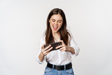 快乐的黑褐色女人玩移动电子游戏 微笑和看着屏幕兴奋 站在白背景上站立人士手机数字职业网络经理成人办公室商务工作图片