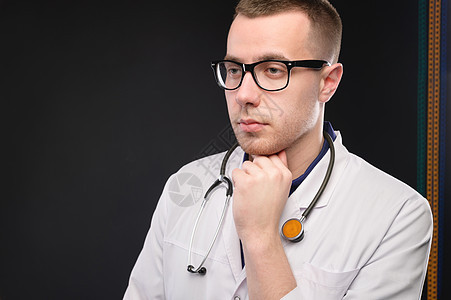 一位戴眼镜 身着白大褂的年轻迷人的白人医生若有所思地站着 向旁边看去 一名护理人员的工作室肖像图片