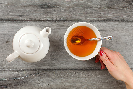 最顶端 年轻女子手与红指甲 握着一杯琥珀茶 和茶壶旁边图片