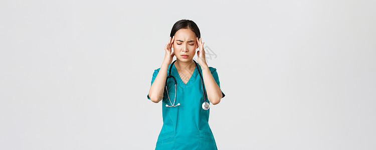 Covid19 医护人员 流行病概念 劳累过度 疲惫不堪的年轻亚洲女护士闭上眼睛 因头痛而做鬼脸 头晕 与冠状病毒患者一起夜班 图片