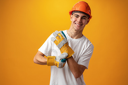 自信的笑着微笑的少年男孩 在黄色背景下戴着橙色硬帽子工作商业建筑师职业幸福建造工作室男生建设者男性图片