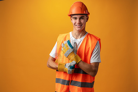 自信的笑着微笑的少年男孩 在黄色背景下戴着橙色硬帽子头盔幸福工业工人男生建设者青少年建筑学工程师建筑师图片