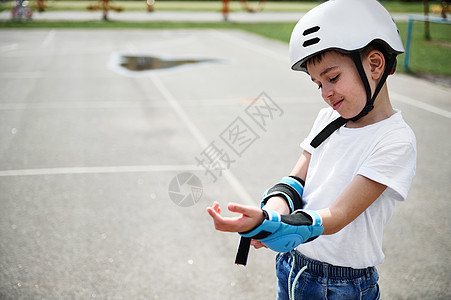 穿着安全头盔的男孩滑板运动员在滑冰前戴上保护性手臂图片