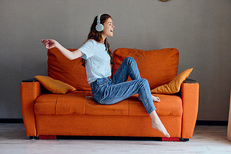 在橙色沙发上的女人 用耳机监听音乐 生活方式图片