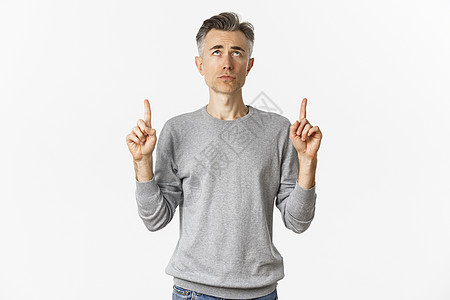 沮丧和犹豫不决的中年男子的肖像 看着烦乱 指着手指举起手来 站立在白背景上不安促销头发灰色工作室毛衣男性广告白色标识商业图片