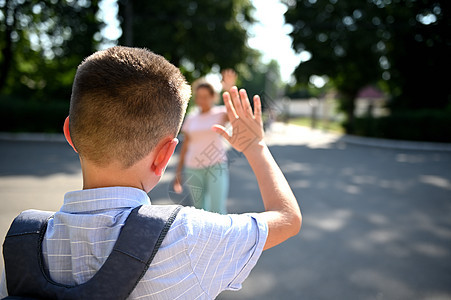 一个小学生站在学校门口 向他模糊的母亲挥手致意 失焦的母亲带她的儿子上学 学年开始图片