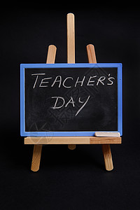 在木制桌边贴上一张粉笔板 上面写着教师节的字母 用黑色背景与复制空间隔绝图片
