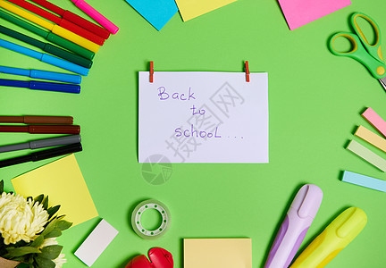 五颜六色的文具办公用品和学校配件的顶部视图排列成一个圆圈 中间是白纸 上面写着回到学校的字样 绿色背景 复制空间图片