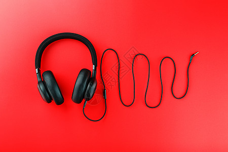 红色背景上的无线黑色耳机 由耳机线制成的声音频率 适合玩游戏和听音乐曲目的入耳式耳机图片