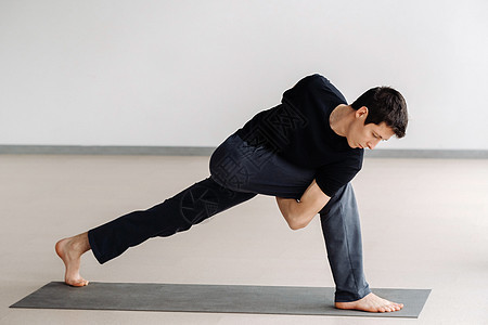 一个穿黑色T恤的男子 站立起来在健身房伸展男人运动护理力量运动垫姿势运动员讲师成人瑜伽图片