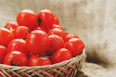 在旧木桌上的柳条篮子里的新鲜红番茄 成熟多汁的樱桃西红柿 上面有几滴水分 灰色的木桌 周围是一块粗麻布 在一个质朴的风格蔬菜水果图片