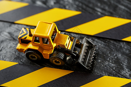 黑色背景纹理上的黄色玩具推土机 在CCCFT背景下的黑黄栅栏胶带车轮击剑金属拖拉机乐趣维修挖掘力量机器技术图片