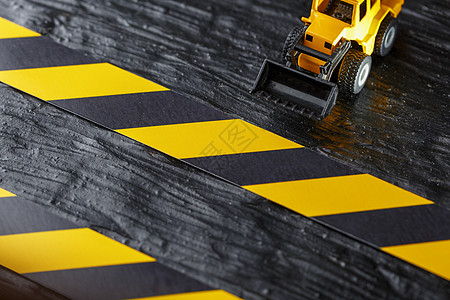 黑色背景纹理上的黄色玩具推土机 在CCCFT背景下的黑黄栅栏胶带车辆维修拖拉机工作击剑装载机塑料技术运输橙子图片