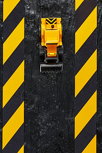 黑色背景纹理上的黄色玩具推土机 在CCCFT背景下的黑黄栅栏胶带橙子击剑金属乐趣挖掘机建造车辆力量磁带工作图片