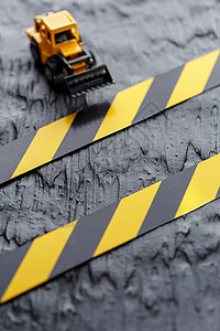 黑色背景纹理上的黄色玩具推土机 在CCCFT背景下的黑黄栅栏胶带橙子车轮车辆力量工作乐趣挖掘机机械磁带塑料图片