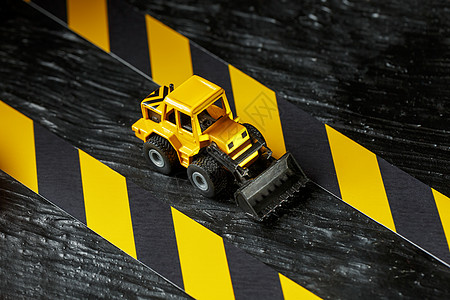 黑色背景纹理上的黄色玩具推土机 在CCCFT背景下的黑黄栅栏胶带建造维修挖掘技术拖拉机力量金属塑料击剑车辆图片