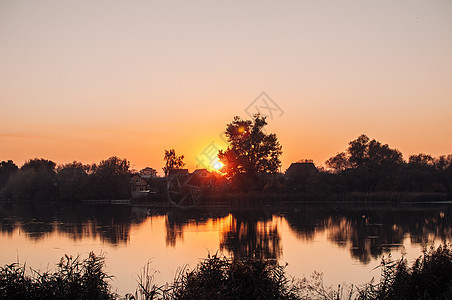 橙色的夕阳映衬着九月收获季节的河流 树木在水中的倒影 美丽的秋天风景 秋天的颜色倒映在平静的水面上蓝色城市地平线太阳海洋游泳天空图片