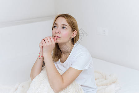 一位年轻女士坐在床上 担心并咬指甲 在卧室的床上坐着临时妇女感到忧虑压力成人手指公寓焦虑女孩女性情绪悲伤房子图片