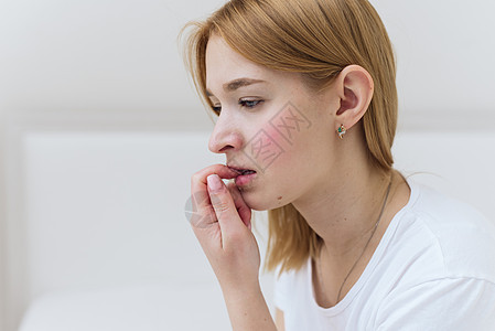 一位年轻女士坐在床上 担心并咬指甲 在卧室的床上坐着临时妇女感到忧虑压力弱点手指黑发女性公寓堕胎房子女孩悲伤图片