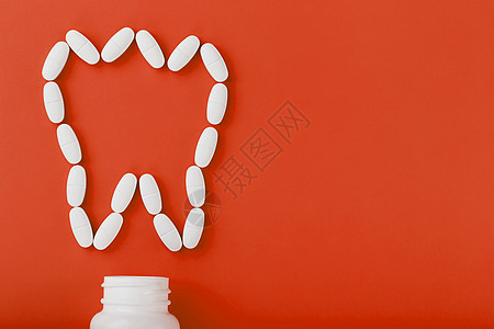 在红色背景上从白罐子里洒出一颗牙状的钙维他命疼痛止痛药制药药店健康剂量银行药品处方治疗图片