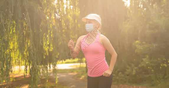 一个运动的年轻女子在户外慢跑 她脸上有防护面具 独自跑着Corona病毒或Covid-19 单独跑来跑去图片