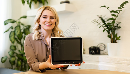 年轻微笑的女士在办公室显示空白平板电脑屏幕 重点放在平板电脑上图片