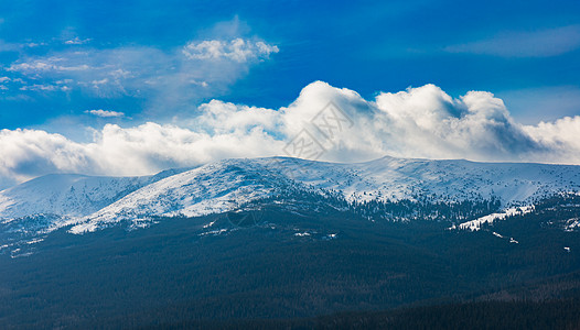 从长远的山脉上看到满是积雪和巨大的云层的浮肿多云风景蓝色岩石旅行高山远距离阴霾顶峰旅游天空图片