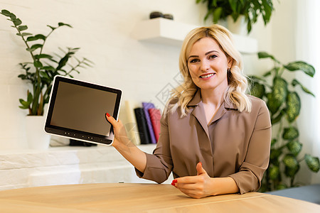 女性展示平板电脑时用空白黑屏幕显示她的照片 然后转而面对照相机进行文字或广告药片相机长椅互联网蓝色微笑购物沙发商业软垫图片