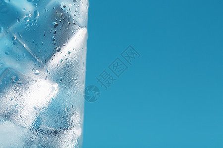 一杯有冰水和冰块的杯子 在蓝色背景上立方体反射气泡水晶液体茶点饮料宏观酒吧白色图片