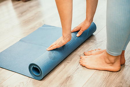女人的手在瑜伽健身训练室的健身房地板上卷起瑜伽垫 在家锻炼的女人合上双手滚动泡沫瑜伽健身垫 女性赤脚家庭锻炼运动健康生活方式概念图片