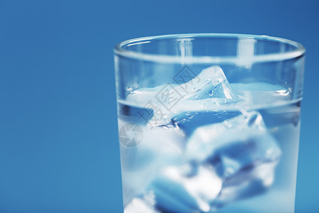 一杯有冰水和冰块的杯子 在蓝色背景上调子液体水晶食物口渴冻结饮料流动瓶子气泡背景图片