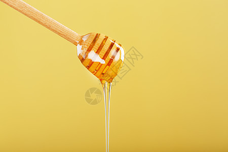 黄色背景的木制蜂蜜花朵上的金色蜂蜜饮食金子蜂窝流动糖浆工具食物营养健康饮食甜点图片