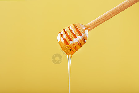 蜜糖从黄色背景的蜂蜜小溪流中滴落饮食食物产品营养毛毛雨早餐木头工具流动甜点图片