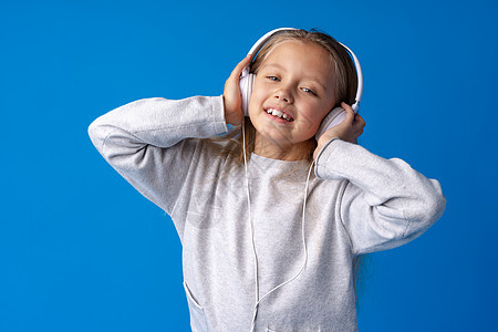 女童戴着耳机 在蓝背景下听音乐女孩戴耳机女孩微笑收音机娱乐喜悦童年快乐乐趣技术衣服图片