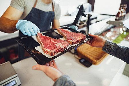 在一家屠夫店里把生肉塞进盘子里猪肉黑色切菜板牛扒盒子托盘熟食食物屠宰场鱼片图片