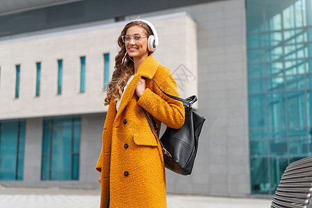 妇女戴眼镜 听音乐 耳语和走出门走出去有声读物外套收音机快乐微笑技术歌曲音乐女子耳机背景图片