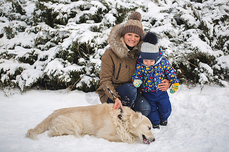 美丽的母亲和儿子在雪地里玩我的狗 金色的寻宝游戏季节友谊猎犬公园女士微笑帽子靴子女性夹克图片