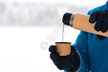 女性用手把热茶或咖啡倒进杯子 从冬季森林的热水池中吐出来 在寒冷的天气下喝着温暖的饮料图片