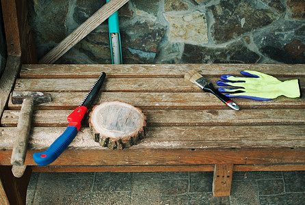 一把旧锤子 一只手锯 防护手套和一张长凳上带锯尘的圆松木束 Wooden代表主班的食物 DIY概念工作手锯活动工业木工红色木头金图片