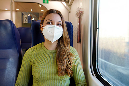 在COVID19世界的城市流动与安全中 快乐的年轻女子戴着医疗面具坐在火车上看镜头 幸运的是机动性学生女孩女士通勤者装备变种旅行图片