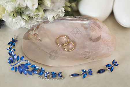 金婚戒贴在蓝色首饰和鲜花旁边的粉红色大理石贝壳上珠宝仪式宝石钻石婚礼花朵桌子惊喜金子展示图片
