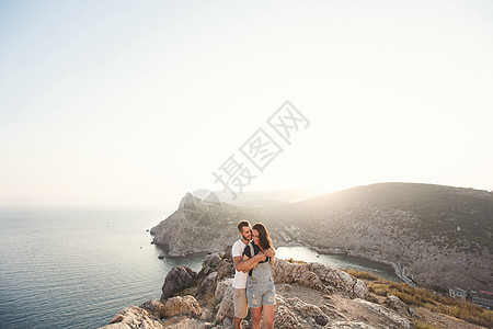 盖伊拥抱一个女孩 在岩石边缘 紧贴在山底的岩壁上悬崖冒险蜜月法帽蓝色女孩海岸日落幸福夫妻图片