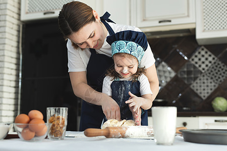 母亲和女儿穿着相配的围裙和厨师帽在厨房里做饭 他们把面团擀开 撒上面粉烹饪女士童年快乐帮手食物蛋糕营养成人父母图片