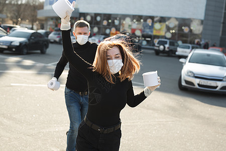 一名身着冠状病毒的妇女和一个男人面罩在城市街道上持有大量手纸 并沉溺其中图片